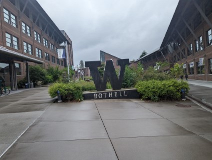 A photo of a large statue of the University of Washington logo, a large, stylized W. The base of the statue is engraved with the text "BOTHELL".