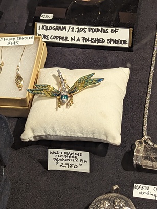 Photo of jewelry, a "gold + diamond cloisonne dragonfly pin" being sold for a whopping $2,750, as the label says. It's a tiny, but very shiny piece of jewelery resting on a little white pillow.