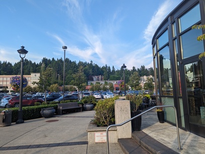 A picture of a parking lot with tall buildings in the distance, along with a hilly landscape lush with green Evergreen trees.